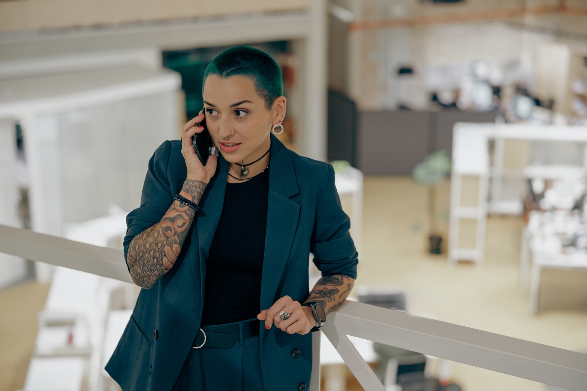 Focused tattooed female business owner is talking mobile phone while standing in modern coworking