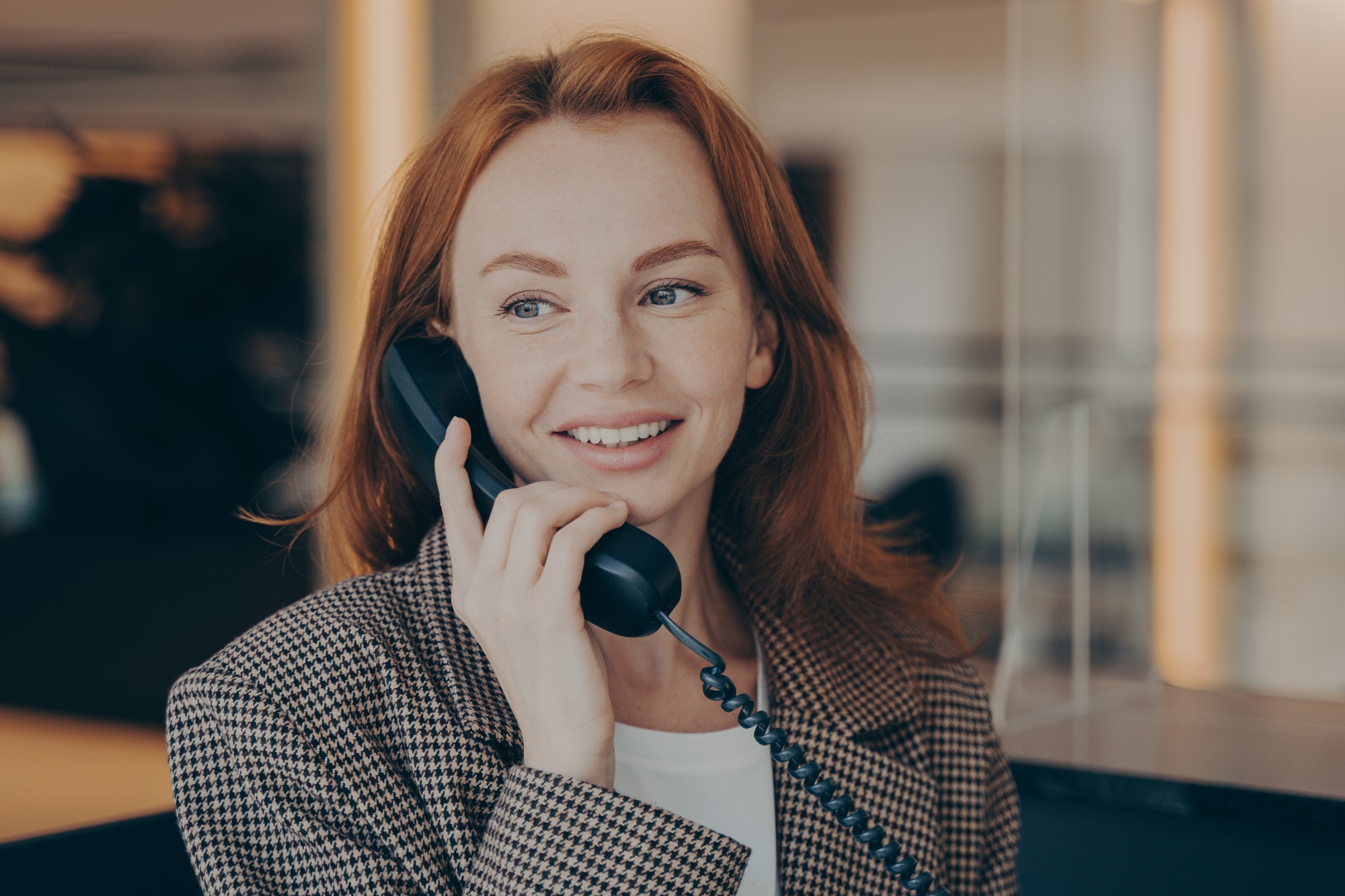 Portrait of satisfied female office worker using black landline phone, calling business partner